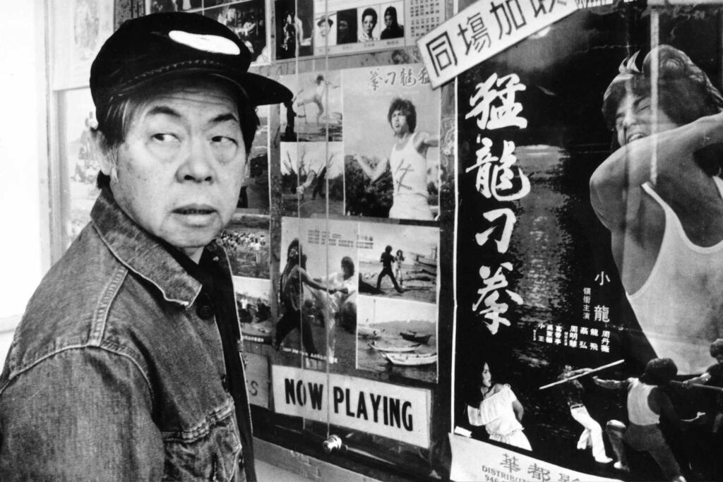 Jo (Wood Moy) stands in front of movie posters.